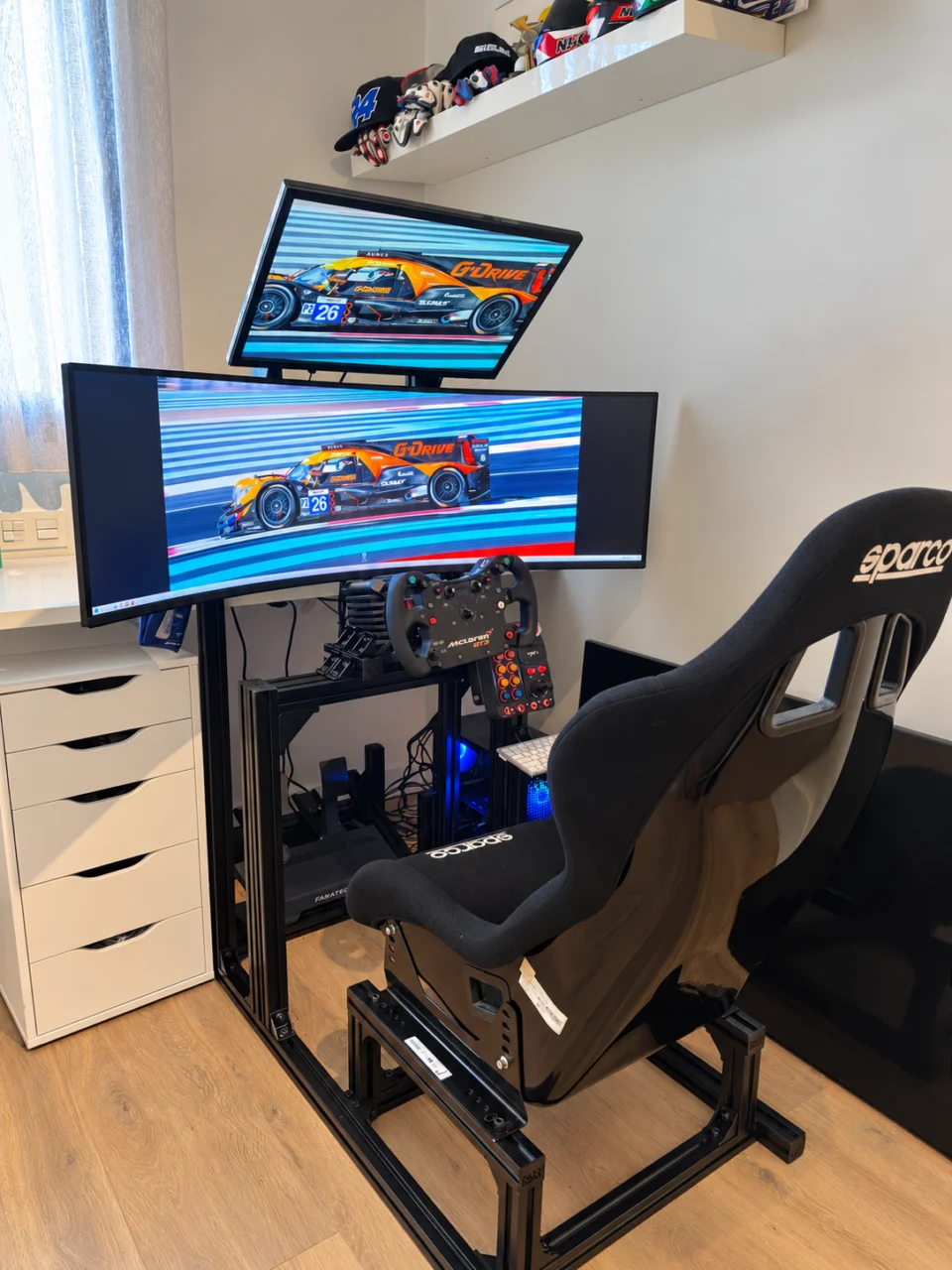 Setup de simracing de un cliente con cockpit negro, asiento Sparco y dos monitores.